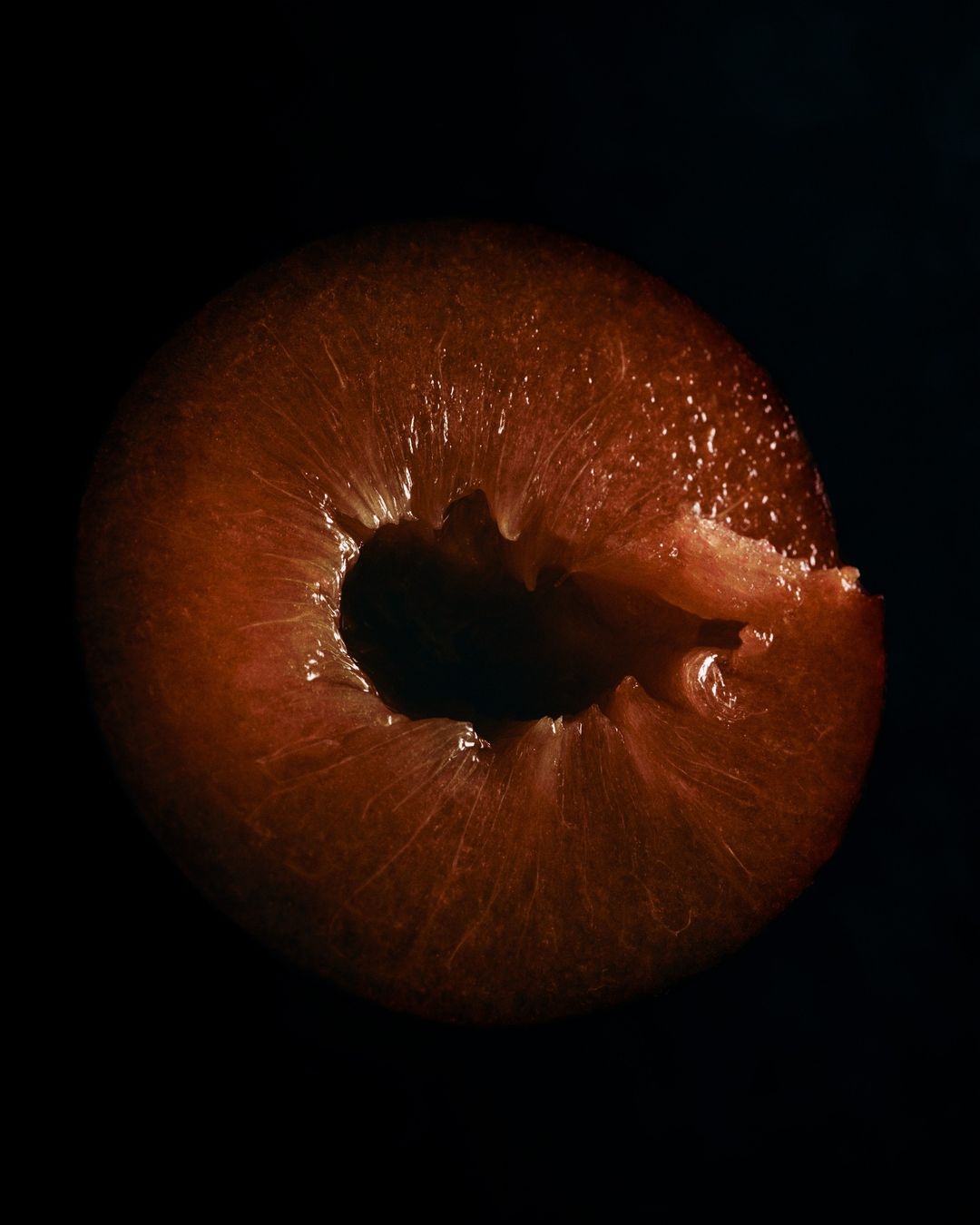 Cross-section of a plum fruit against a black background, showcasing its vibrant color and intricate internal structure in studio lighting.
