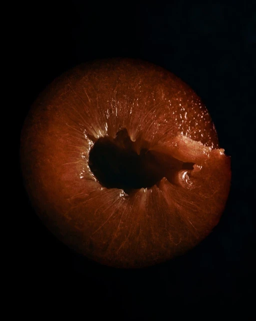 Cross-section of a plum fruit against a black background, showcasing its vibrant color and intricate internal structure in studio lighting.
