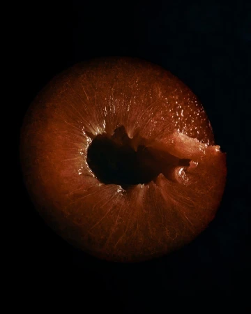 Cross-section of a plum fruit against a black background, showcasing its vibrant color and intricate internal structure in studio lighting.