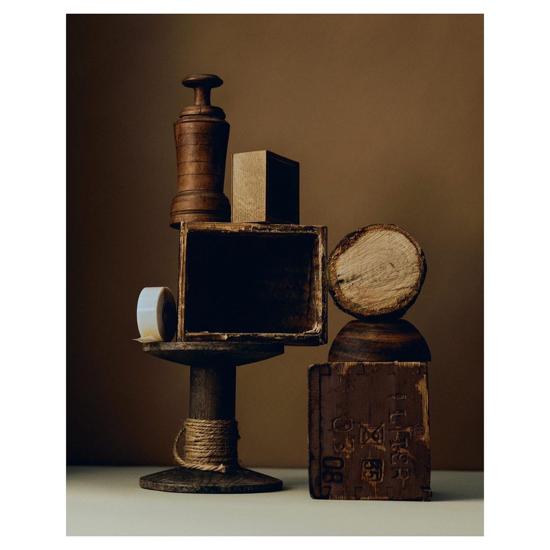 Still life arrangement of wooden objects including cube, spool, box, log against a brown background, showcasing textures and forms.