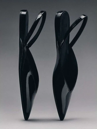 Two black patent leather slingback flats standing upright against a seamless neutral grey studio background.