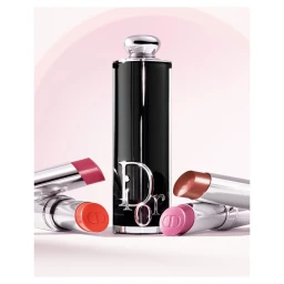 Close-up product photograph of a black Dior lipstick tube standing vertically surrounded by four open lipsticks in varying pink, coral, and nude shades.
