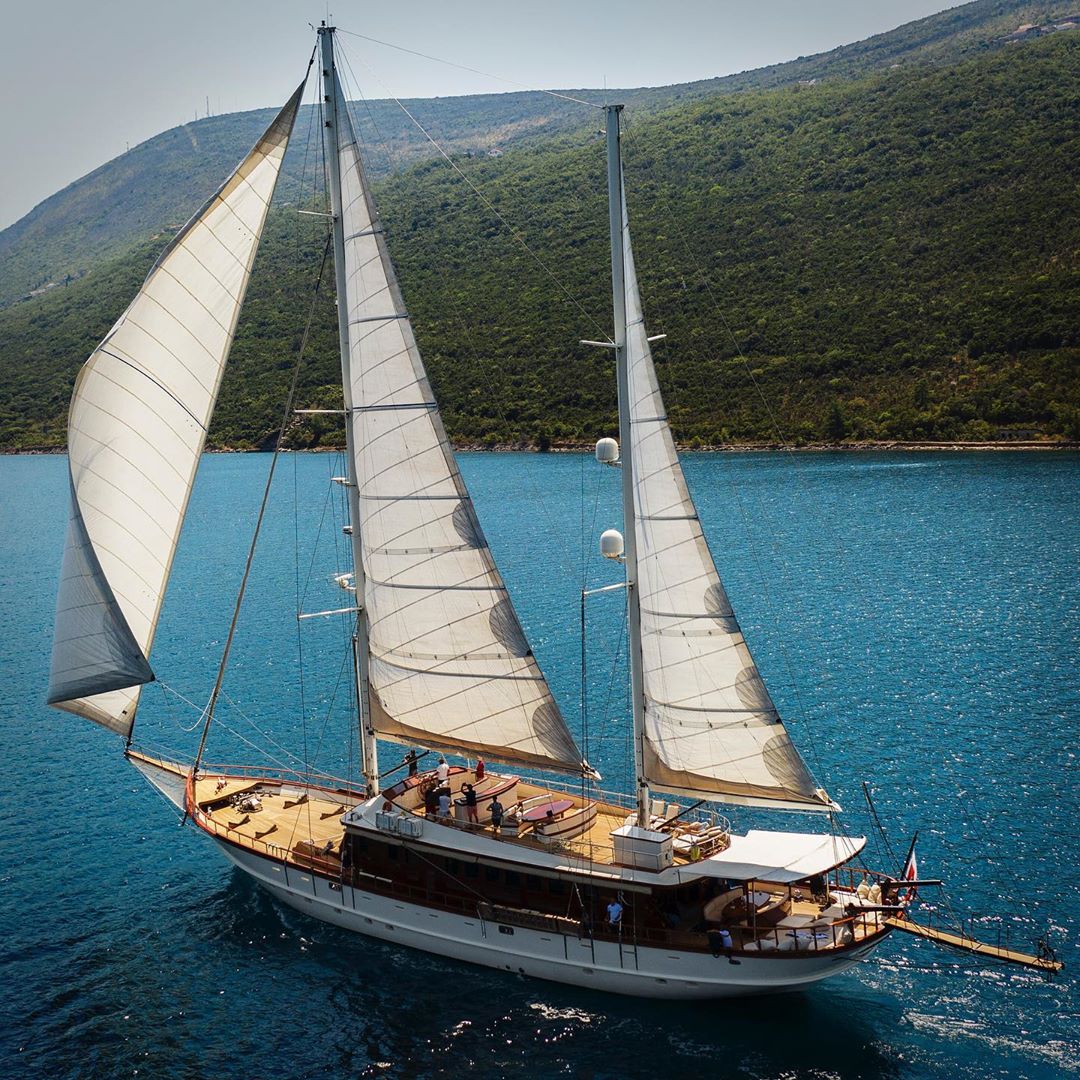 Sailing yacht gliding on blue ocean waters, backed by green hills, capturing a blend of maritime adventure and scenic beauty on the sea.