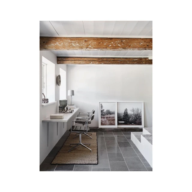 Minimalist interior with white walls, wooden beams, and two landscape art prints, complemented by gray tiled flooring and neutral rug.