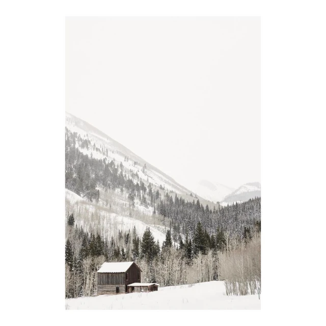 Snow-covered barn sits amidst pine trees and snow-dusted mountains, creating a serene winter landscape.