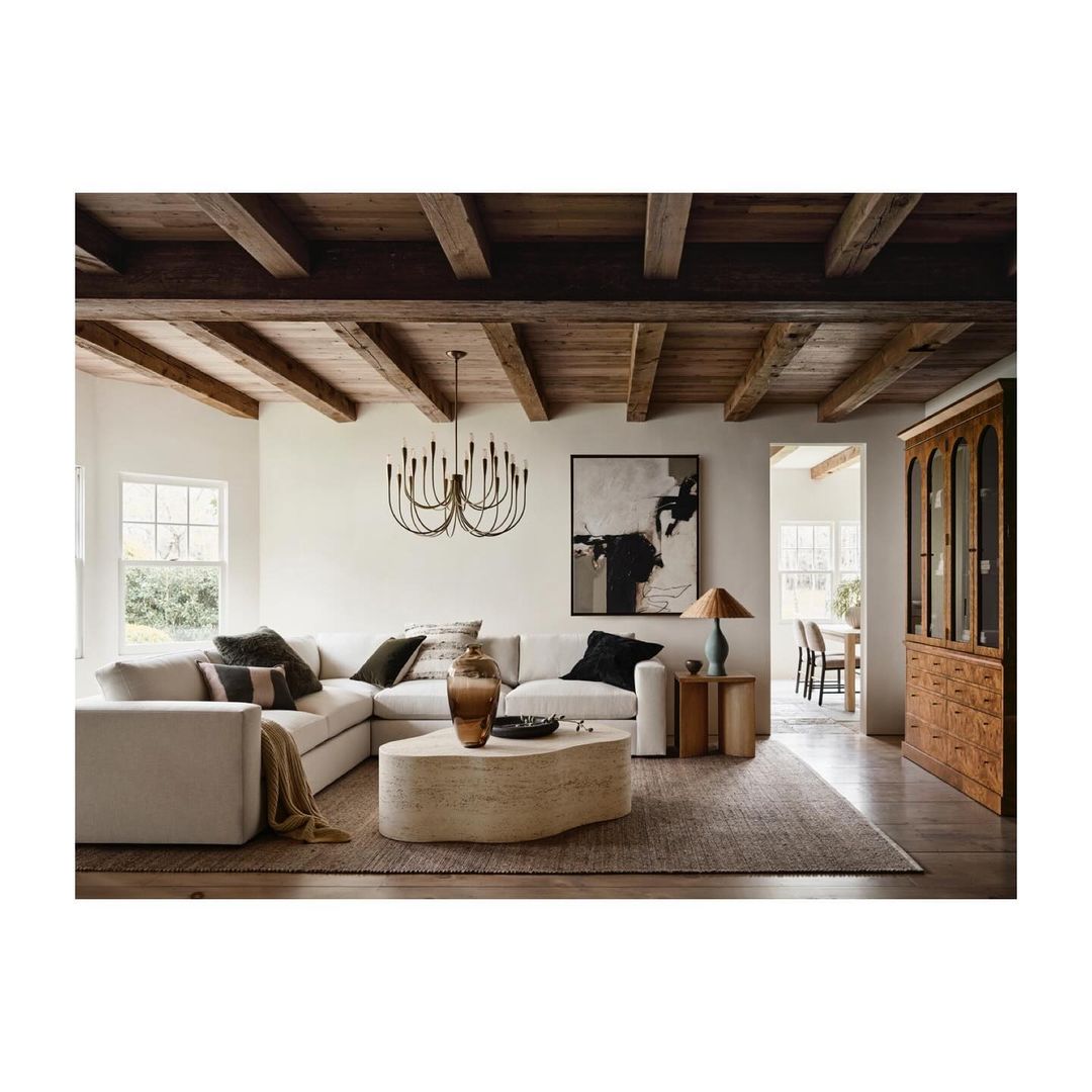 Living room interior with a sectional sofa, a stone coffee table, and a modern chandelier, lit by natural light from windows.
