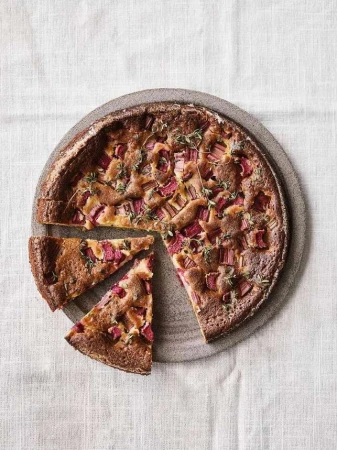 Overhead shot of a rhubarb cake with thyme on a round gray plate with two slices cut out, placed on a white linen tablecloth.