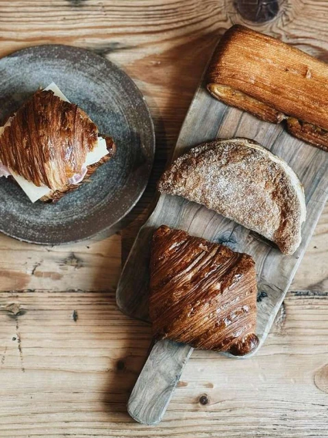 Overhead shot of assorted pastries including croissants and danishes arranged on a wooden surface with rustic plates and boards.