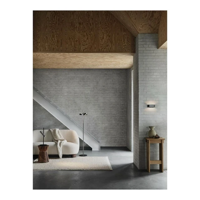 Living room interior featuring a light-colored sofa, a small side table, a modern floor lamp, and light grey brick wall details.