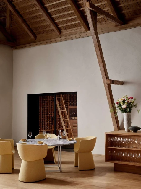 Interior of a dining room featuring a marble table with yellow chairs, wooden floors, and a wine cellar in the background.