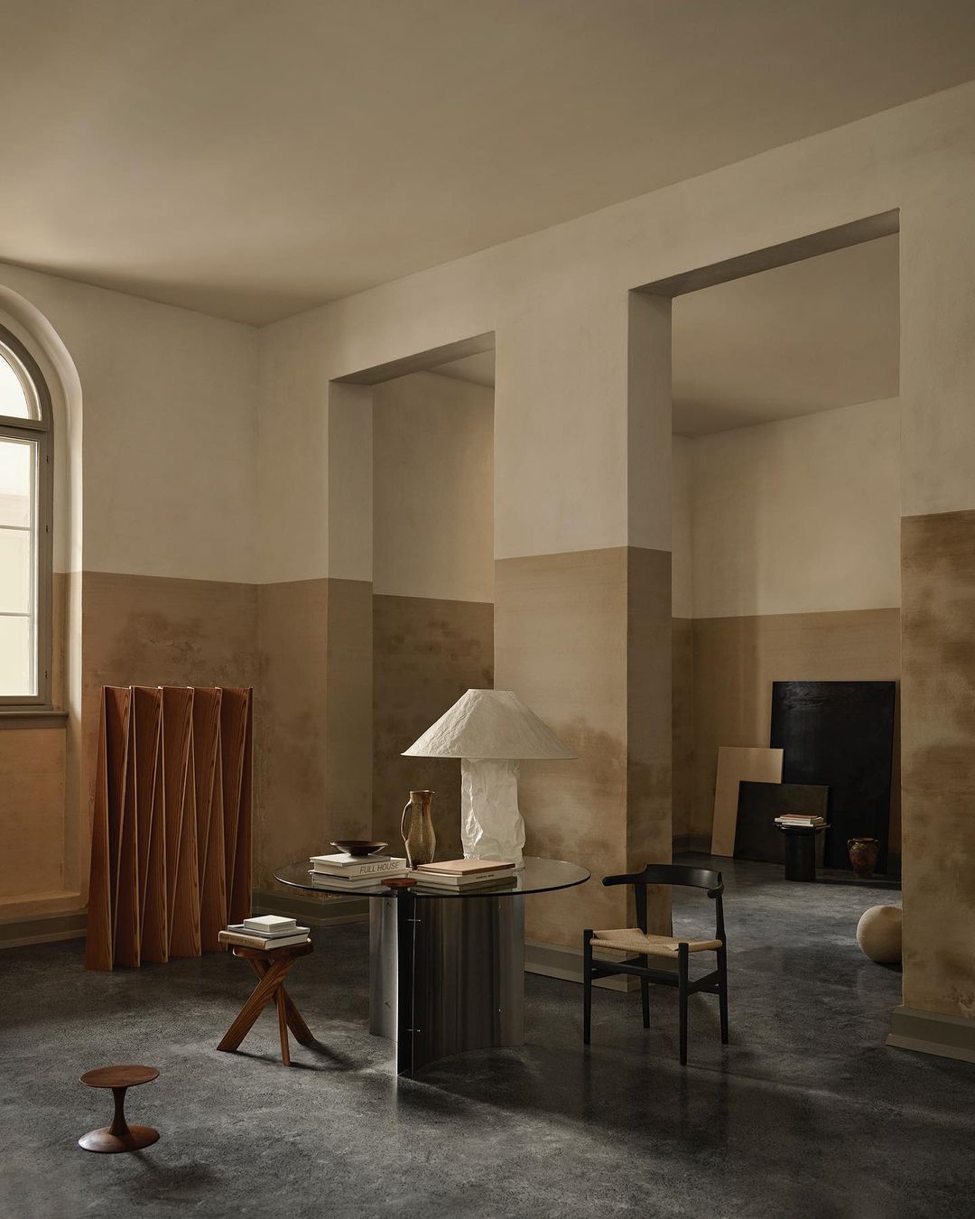 Neutral interior featuring a modern round table with a lamp, a woven chair, and warm color scheme. Minimalist design.