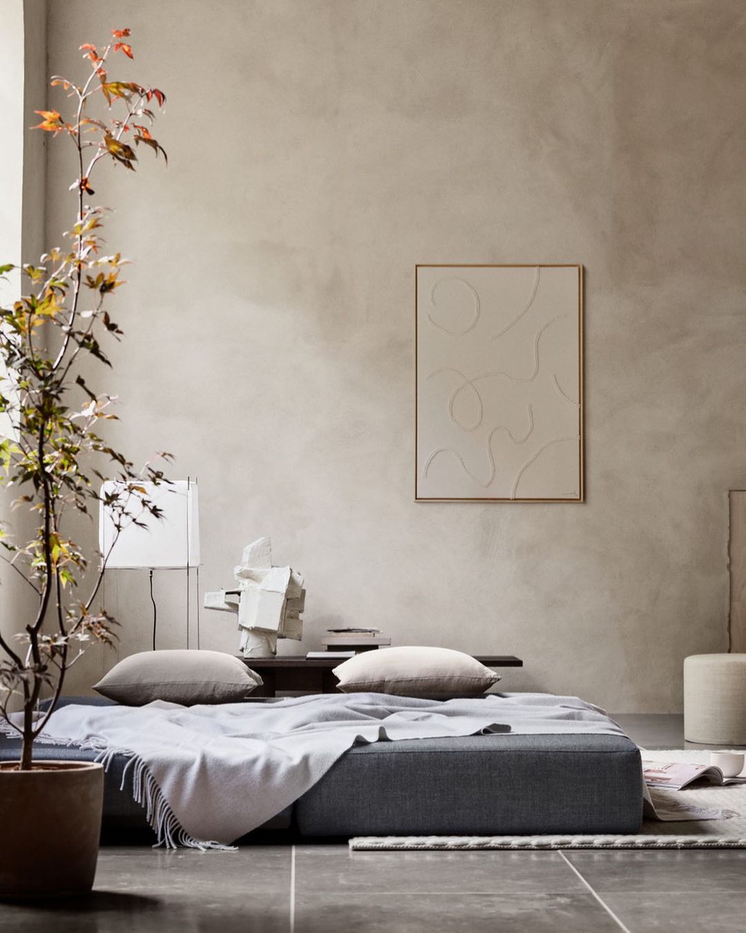 Beige interior with a gray sofa, pillows, a framed art piece, a potted plant, and soft, neutral lighting creates a cozy atmosphere.