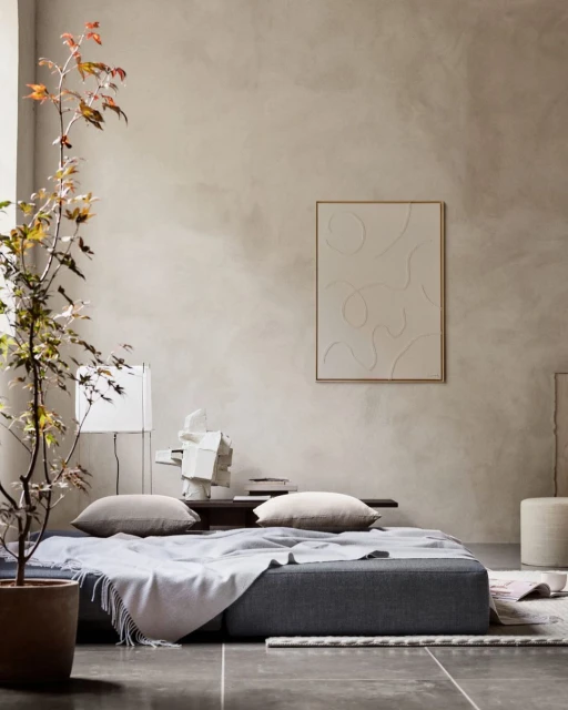 Beige interior with a gray sofa, pillows, a framed art piece, a potted plant, and soft, neutral lighting creates a cozy atmosphere.