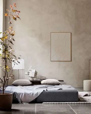 Beige interior with a gray sofa, pillows, a framed art piece, a potted plant, and soft, neutral lighting creates a cozy atmosphere.
