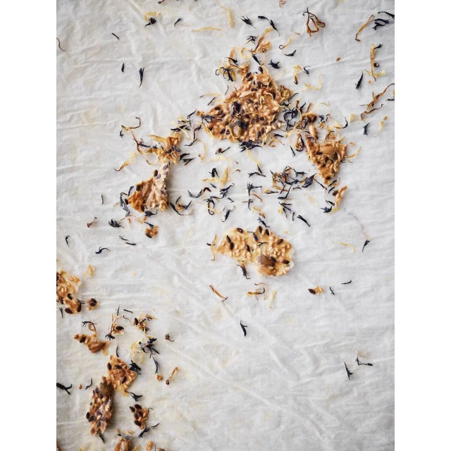 Overhead shot of crackers and loose herbs scattered on parchment paper, highlighting textures and organic presentation.