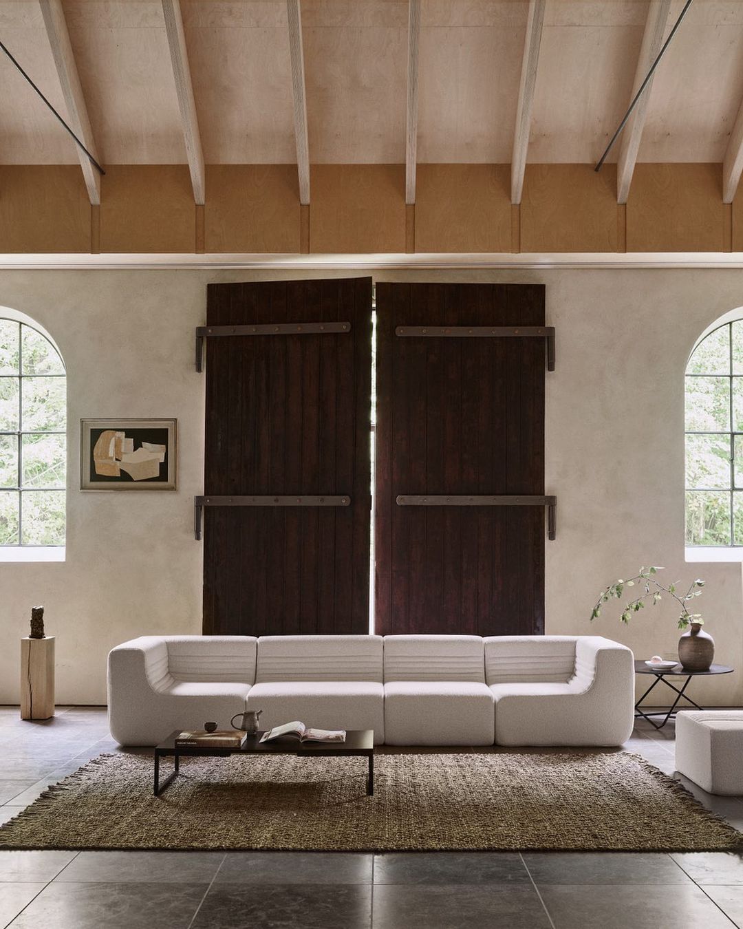 A bright living room interior featuring a modular white sofa, rug, coffee table, and windows providing natural light, creating a minimalist design.