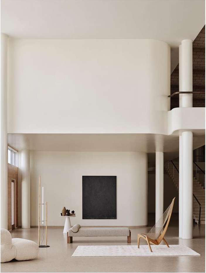 Bright, naturally lit room with neutral tones, featuring a daybed, sculptural chair, modern art, and minimalist decor for an airy, spacious ambiance.