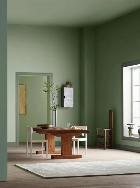 Interior of a dining room featuring a wooden table, chairs, a gray rug, and minimalist decor, all set against an olive green color scheme.