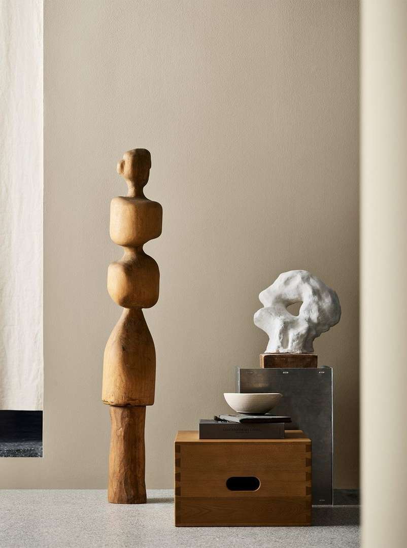 Two abstract art sculptures, one is wood and the other is white, set on platforms in a neutral interior with soft, diffused lighting.