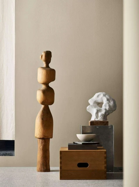 Two abstract art sculptures, one is wood and the other is white, set on platforms in a neutral interior with soft, diffused lighting.