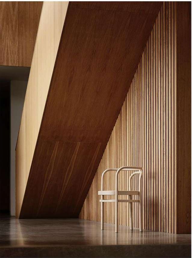 Minimalist interior with a light wood chair against a slatted wood wall, accented by strong diagonal lines from overhead architectural elements.