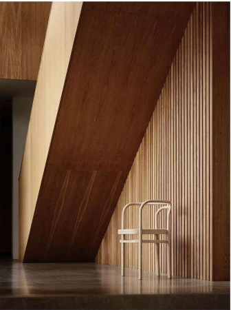 Minimalist interior with a light wood chair against a slatted wood wall, accented by strong diagonal lines from overhead architectural elements.