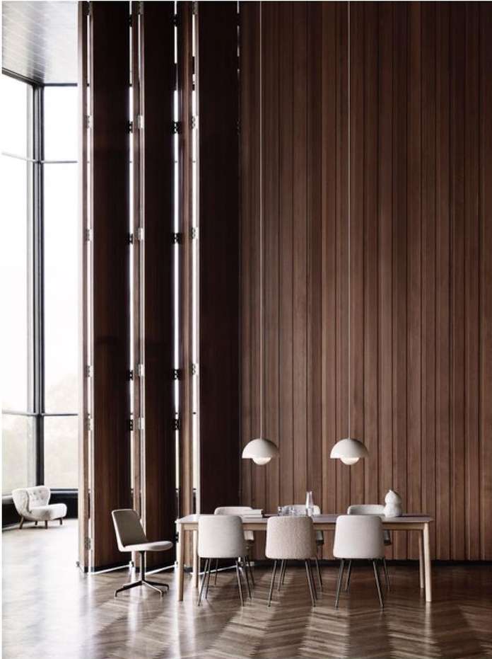 Interior view of a dining room with light-colored chairs around a table, pendant lights, wood-paneled walls, and herringbone floor.