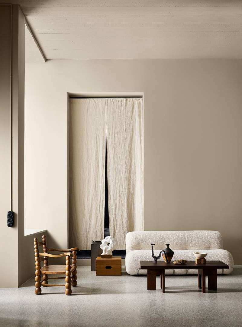 Interior shot with cream-colored walls, a wooden chair, a white couch, and a dark wood coffee table with decorative items.