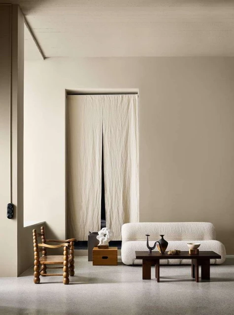 Interior shot with cream-colored walls, a wooden chair, a white couch, and a dark wood coffee table with decorative items.