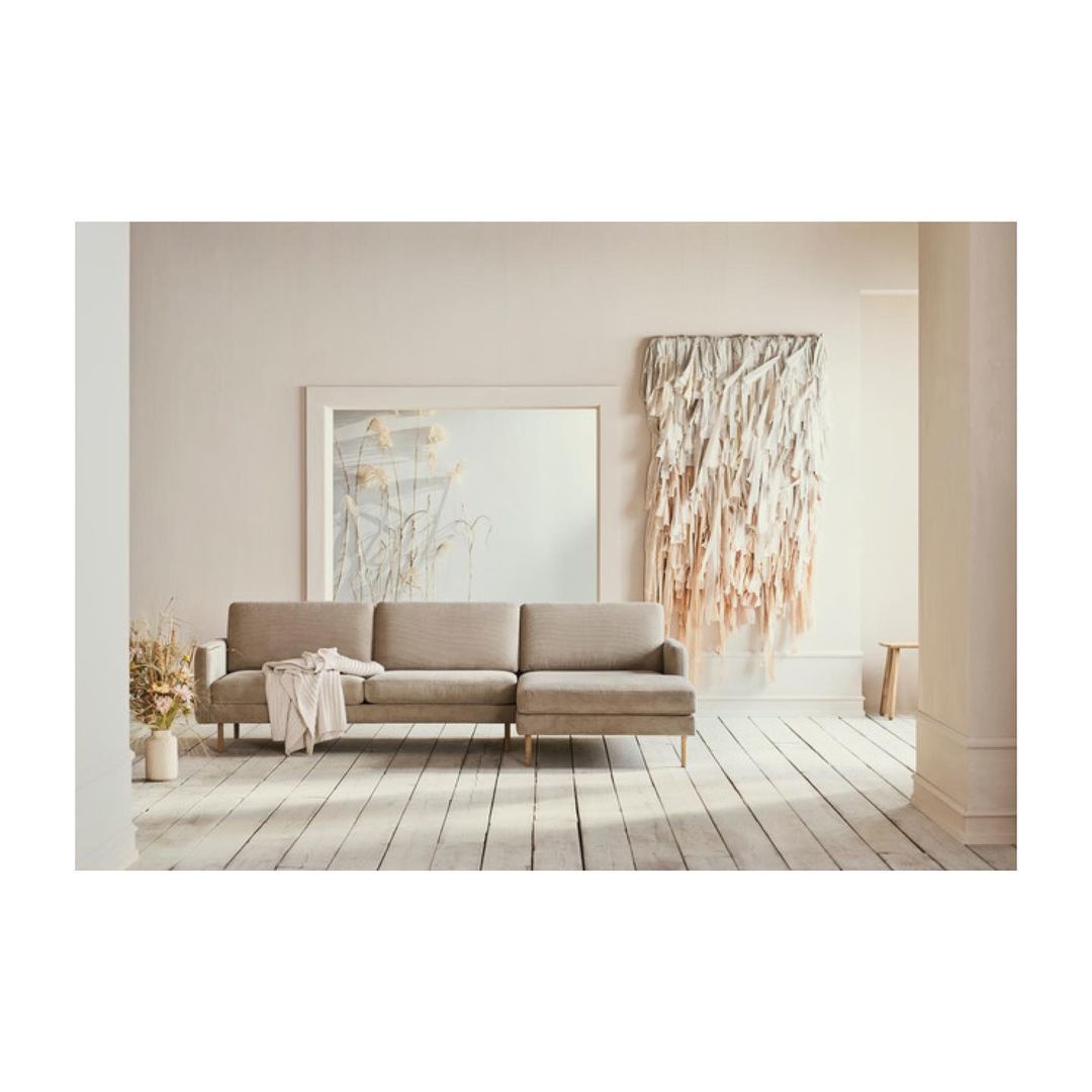 Beige sectional sofa with throw blanket in a light and airy living room with white walls, wood floor, decorative wall art, and flower arrangement.