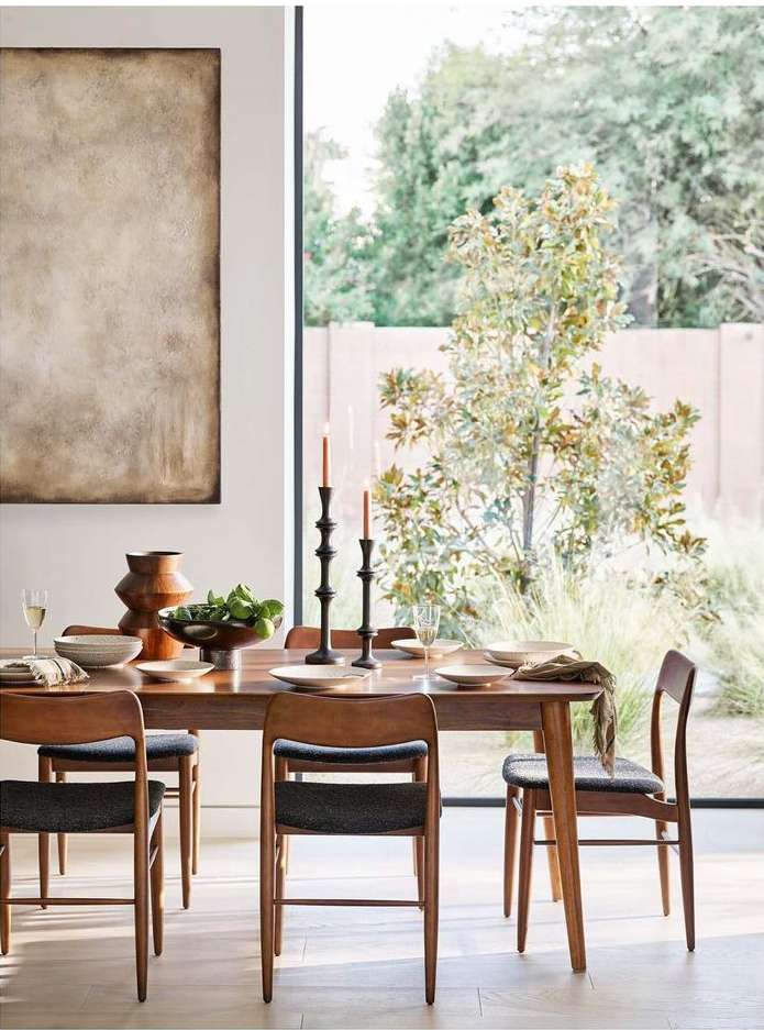 Dining room interior with a wooden table set for a meal, surrounded by wooden chairs, with a window overlooking lush greenery.