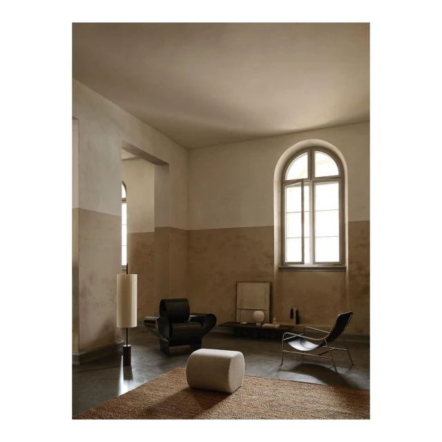 Beige and cream colored living room showcases a black lounge chair, metal framed chair, cylindrical lamp, and light beige ottoman.
