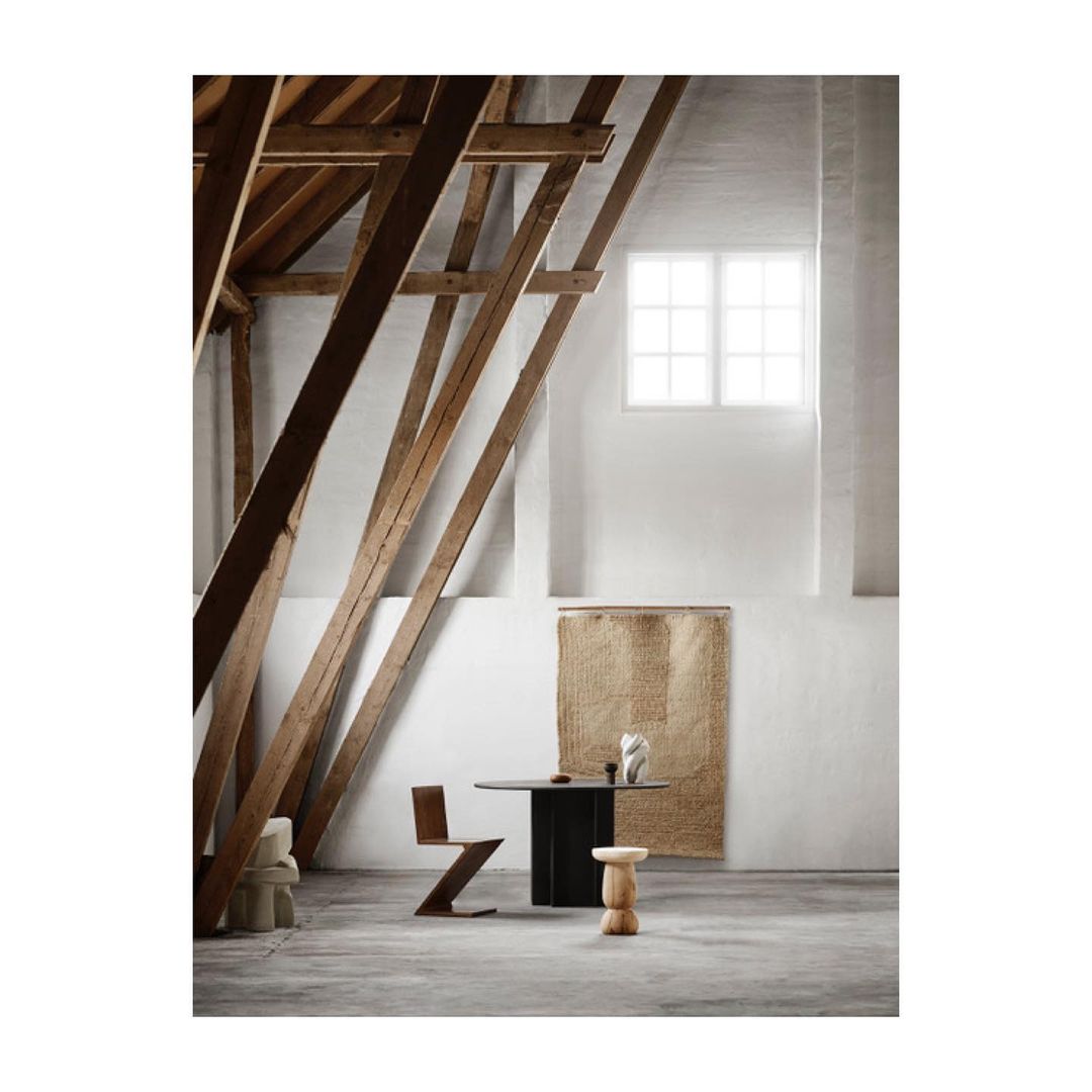 Interior design featuring a modern wooden chair and stool next to a black table in a bright room with exposed wooden beams.