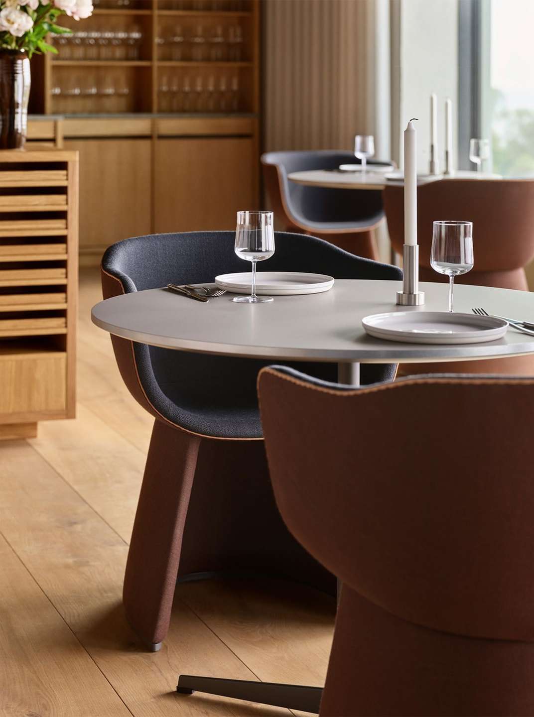Modern restaurant interior featuring round tables with plates and glasses, surrounded by stylish chairs and soft, natural lighting.
