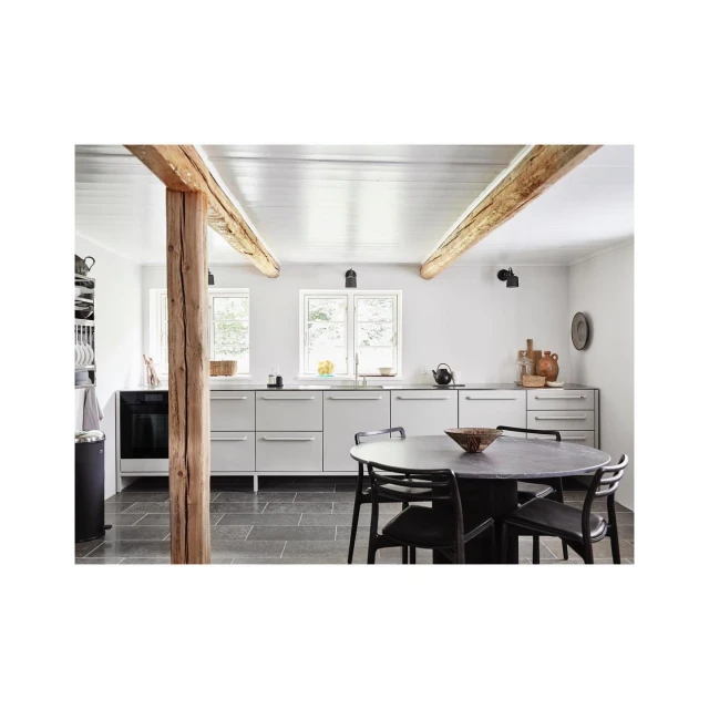Modern kitchen interior with gray cabinets, wooden beam, round table, and black chairs showcasing stylish home design.