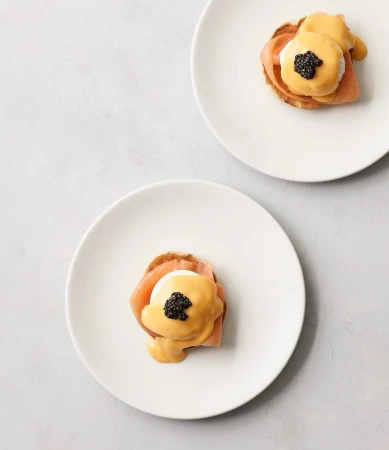 Two plates of eggs Benedict with smoked salmon and caviar sit on a white surface in a simple, minimalist food presentation.