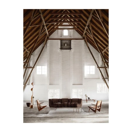 Spacious interior of a converted barn with exposed wooden rafters and white brick walls, featuring a low dark sofa and wooden armchairs.