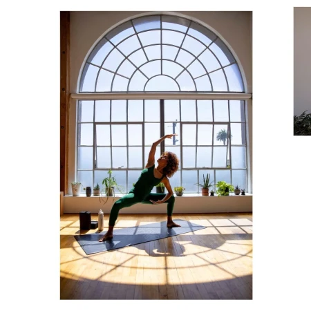 Woman practices yoga in green athletic wear on a mat in a sunlit room with large arched window and plants in a fitness lifestyle scene.
