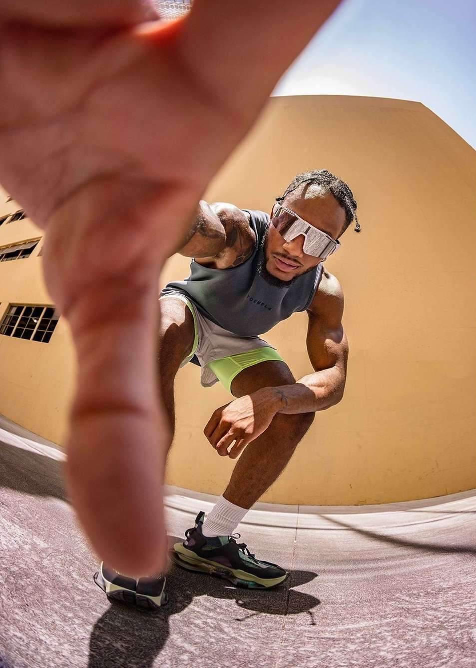 Fish-eye lens photograph featuring a black man in a grey athletic tank top and white shorts reaching toward the camera.