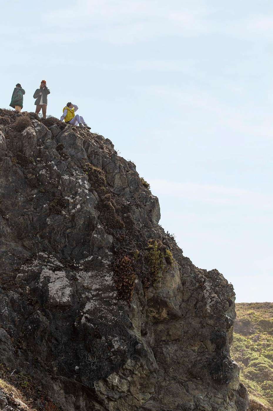 A group of people on a rocky cliff overlooking the ocean under a clear sky, captured in a wide shot showcasing the landscape.
