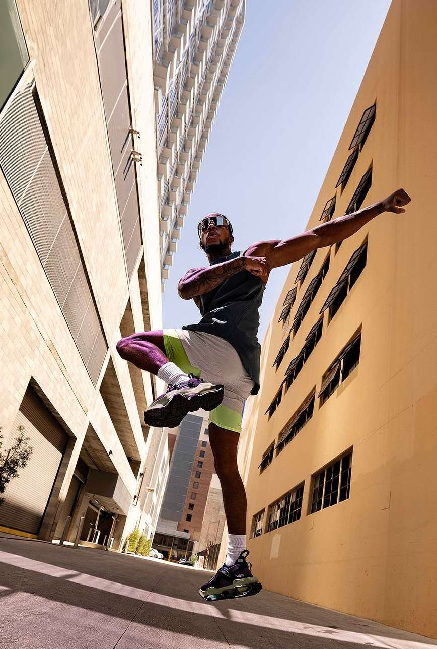 Athletic Black man in sportswear dynamically poses outdoors between tall buildings, showcasing fitness and urban athleticism in natural light.