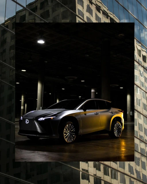 Silver Lexus RZ 450e SUV in a dimly lit parking structure with an office building reflecting in the shot's foreground.