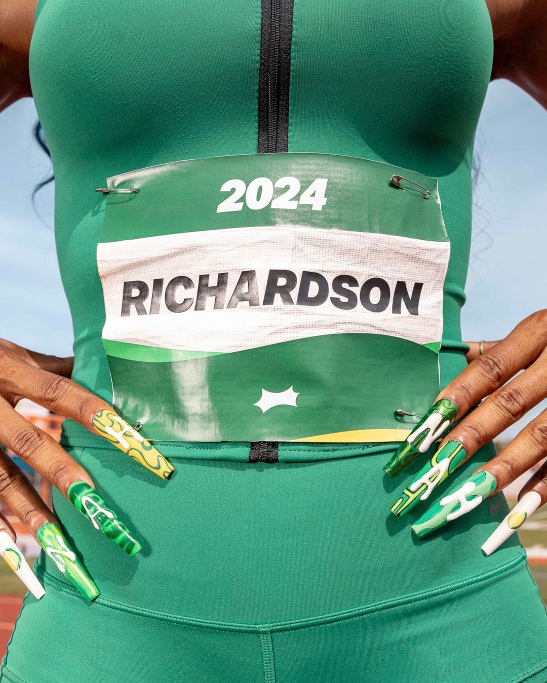 Close-up of an athlete in a green uniform with a racing bib that reads 'Richardson' and '2024,' showcasing her manicured nails.