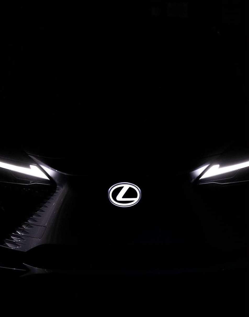 Front view of a black Lexus car with the brand logo in the center and bright white headlights illuminating the vehicle's design.