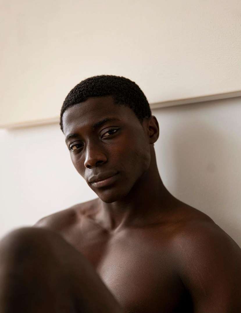 Striking portrait of a shirtless African American man with dark hair against a soft cream backdrop, showcasing natural beauty.