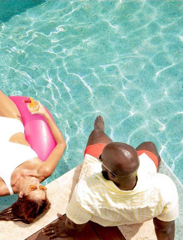 Overhead shot of a man and woman relaxing by the pool on a sunny day, enjoying refreshing beverages and soaking up the sun.