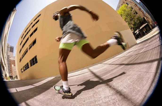 A person runs down a city street past buildings, using a fisheye lens to create a distorted perspective of their outdoor workout.