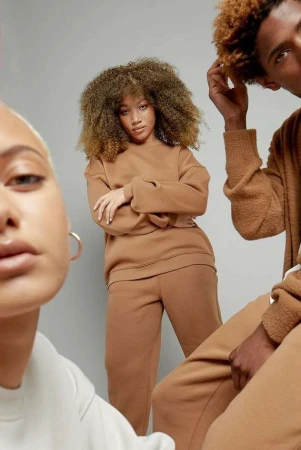 Three models in matching brown outfits posing against a plain grey studio backdrop photographed by Andre L Perry