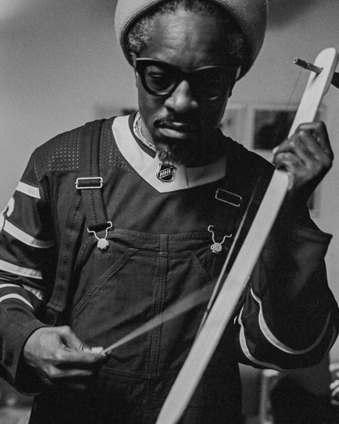 Monochrome portrait of an adult male wearing overalls and a sports jersey, playing a stringed musical instrument, showcasing musical expression.