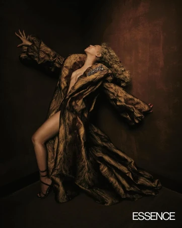 Woman in a dramatic gold textured coat posing in a dark corner against a textured brown wall by photographer Andre Wagner.